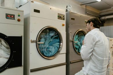 A man is standing in front of a washing machine in a laundromat.