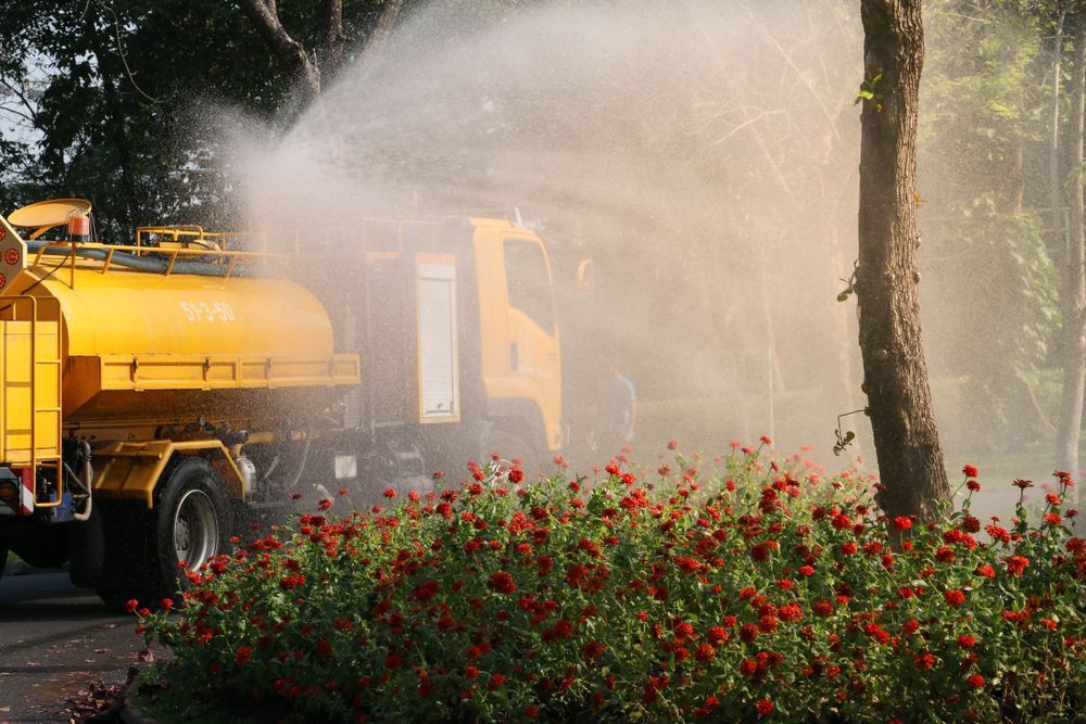 Yellow Water Truck Spraying Water on Red Flowers and Trees — Summit Tree Services in Glenwood, QLD