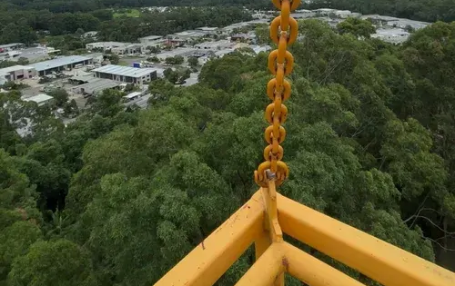 Yellow Chain Hangs From a Yellow Railing Overlooking a Green Forest and Town — Summit Tree Services in Coolum, QLD