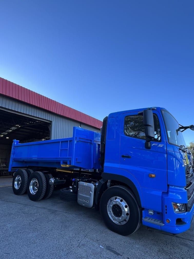 A blue dump truck is parked in front of a building.