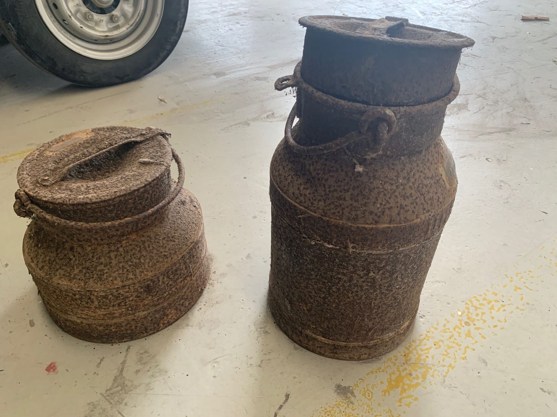 Two rusty cans are sitting next to each other on the floor.