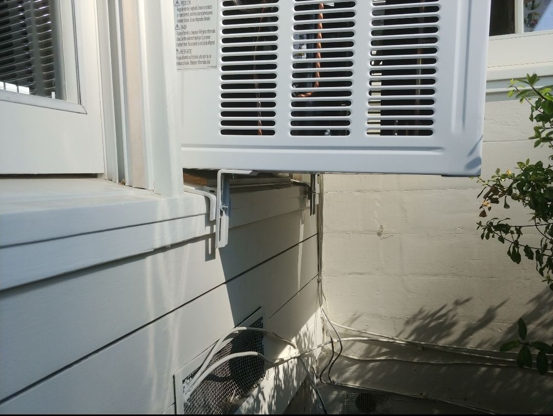 A white air conditioner is mounted to the side of a building