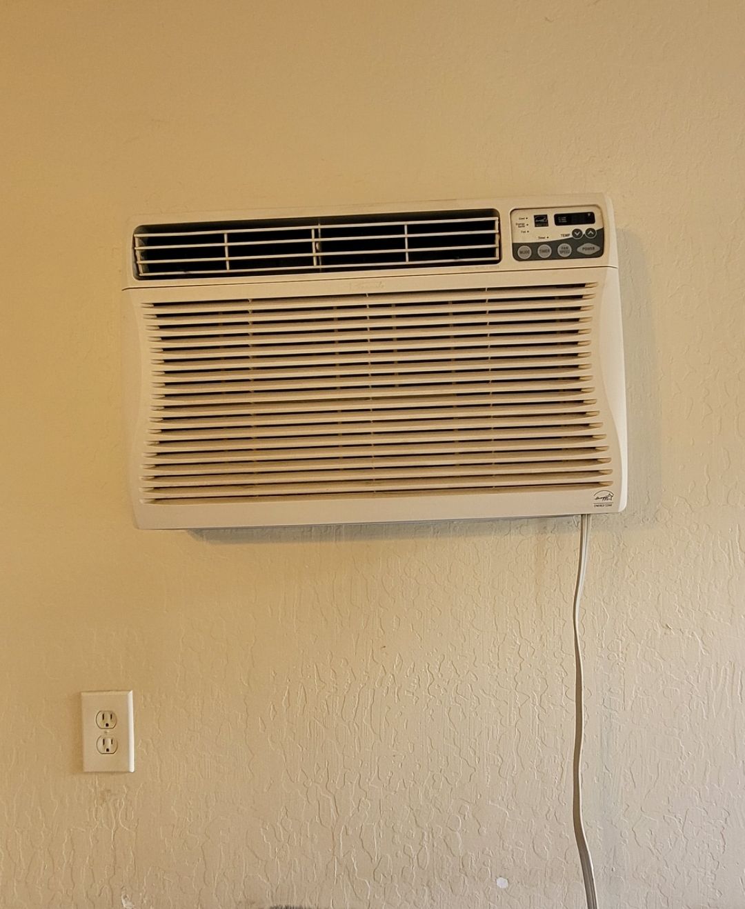 A white air conditioner is hanging on a white wall.