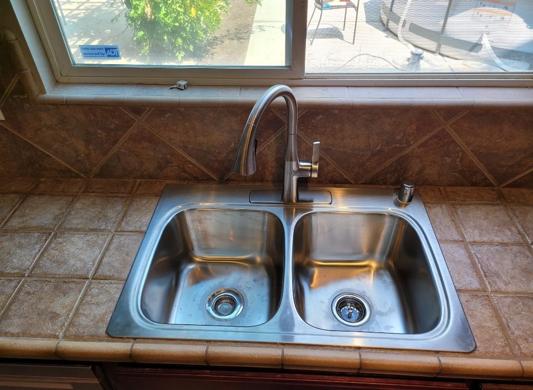 A stainless steel kitchen sink with a window in the background