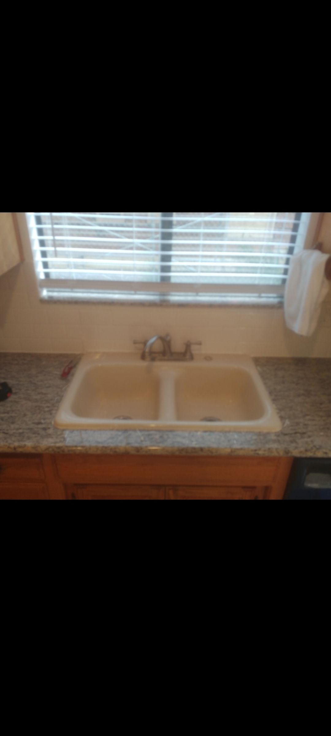 A kitchen sink is sitting under a window with blinds.