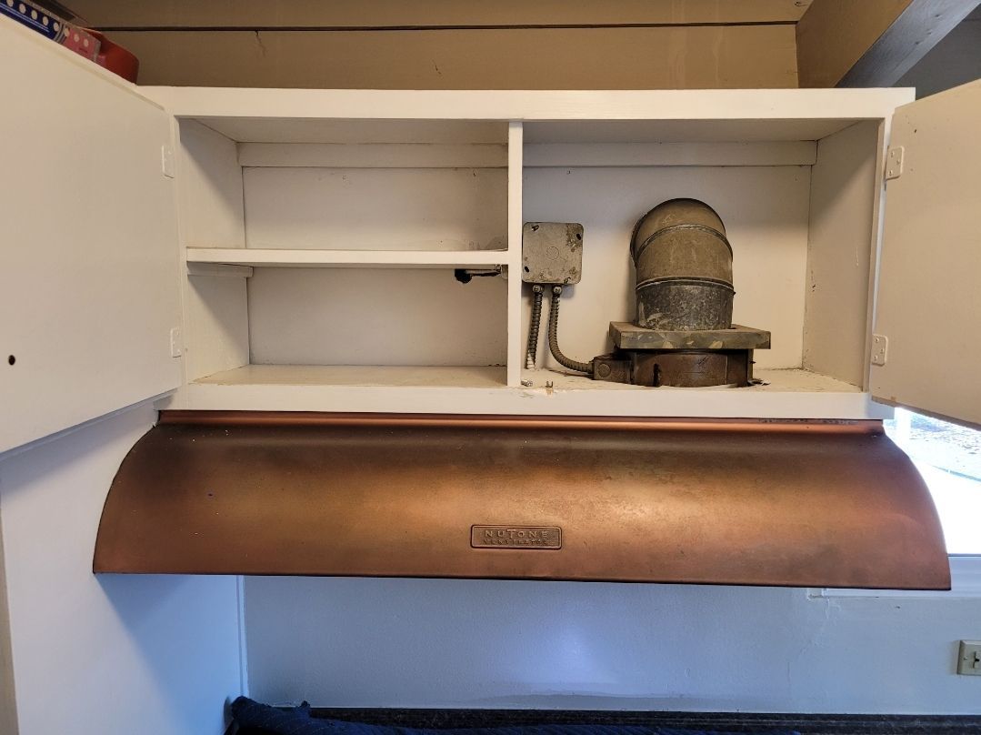 A copper hood is hanging above a white cabinet in a kitchen.