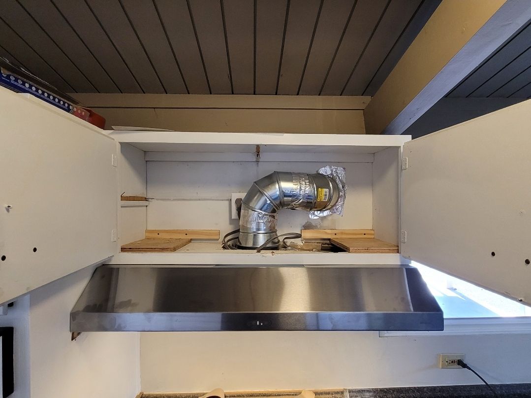 A stainless steel hood is hanging from the ceiling in a kitchen.