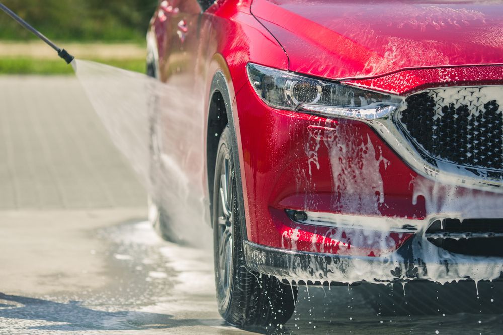 A Red Car Is Being Washed with A High Pressure Washer — Platinum Hand Car Wash & Detailing in Belconnen, ACT