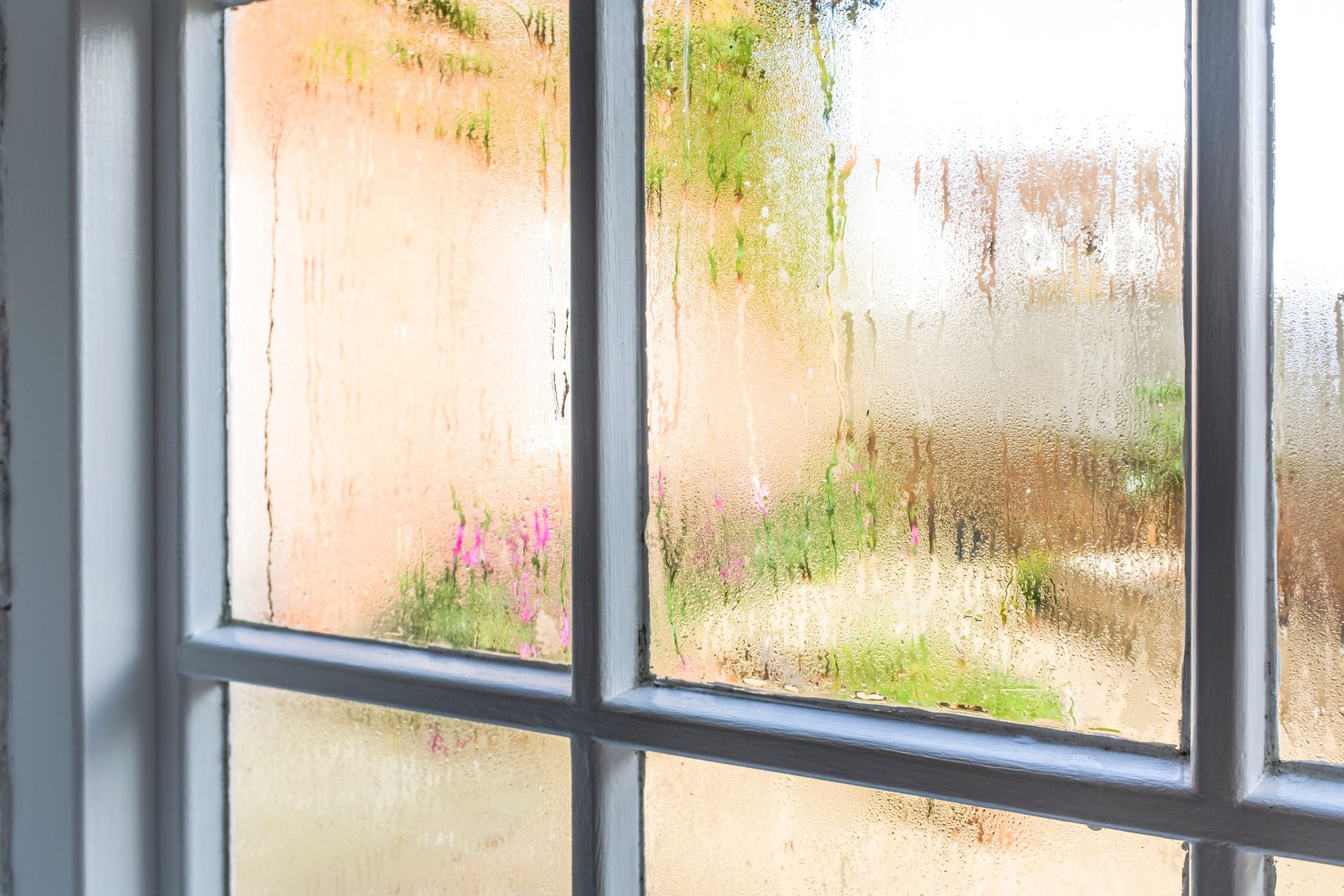 Rain-speckled window panes overlooking a blurred garden and pink flowers