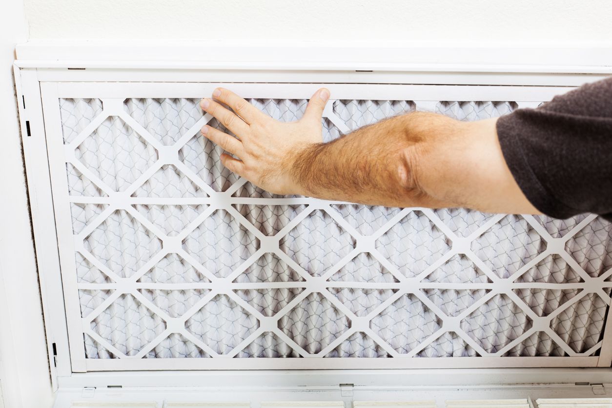 Hand reaching toward a white air filter in a wall vent opening
