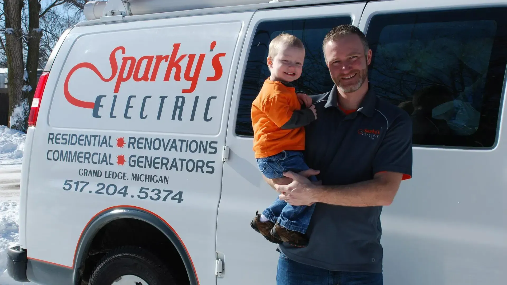 A man is holding a child in front of a sparky 's electric van.