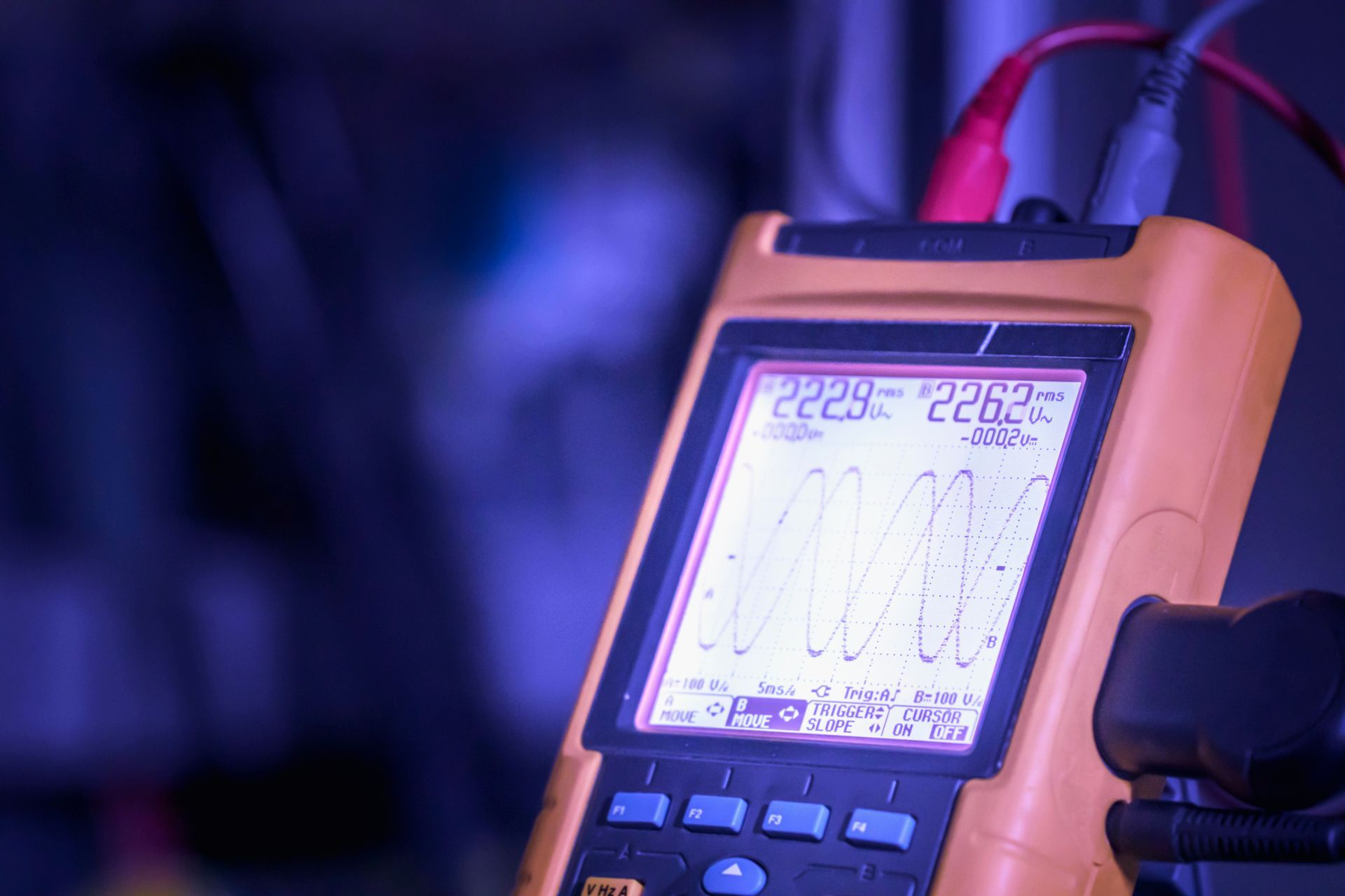 Portable electronic meter with a lit screen showing a wave graph, held in a dark setting