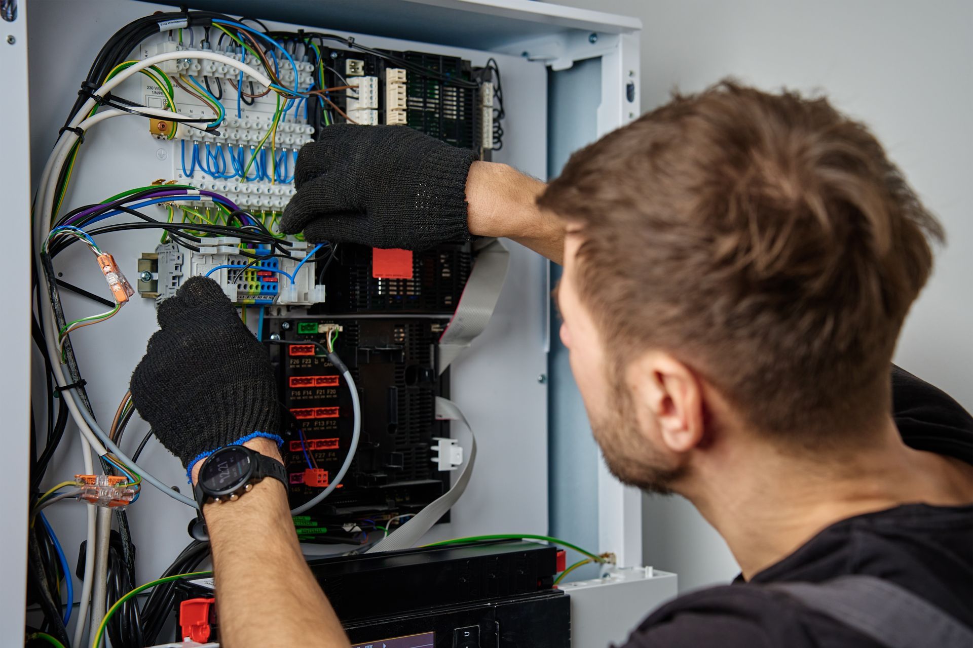 Technician wiring an open electrical control panel with multicolored cables and tools