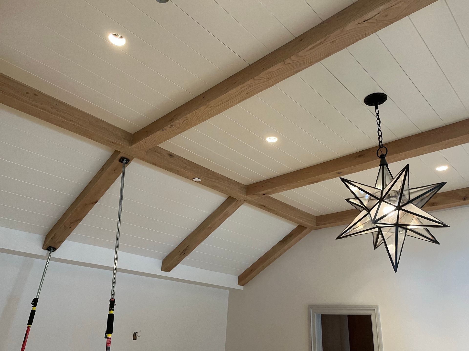 White vaulted ceiling with wooden beams, recessed lights, and a black star-shaped hanging pendant light.