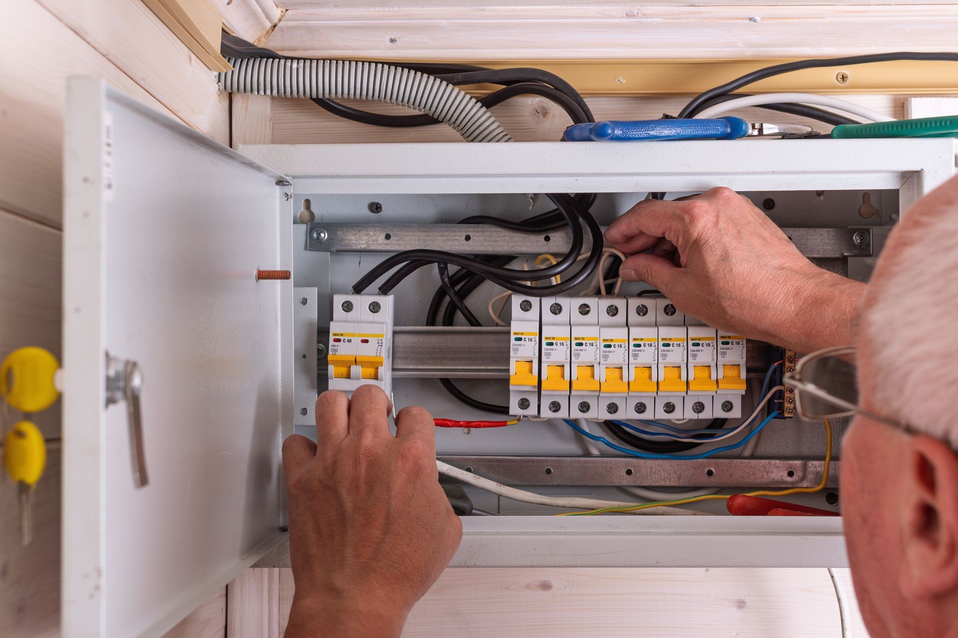 Hands working inside an open electrical control panel with circuit breakers and wiring