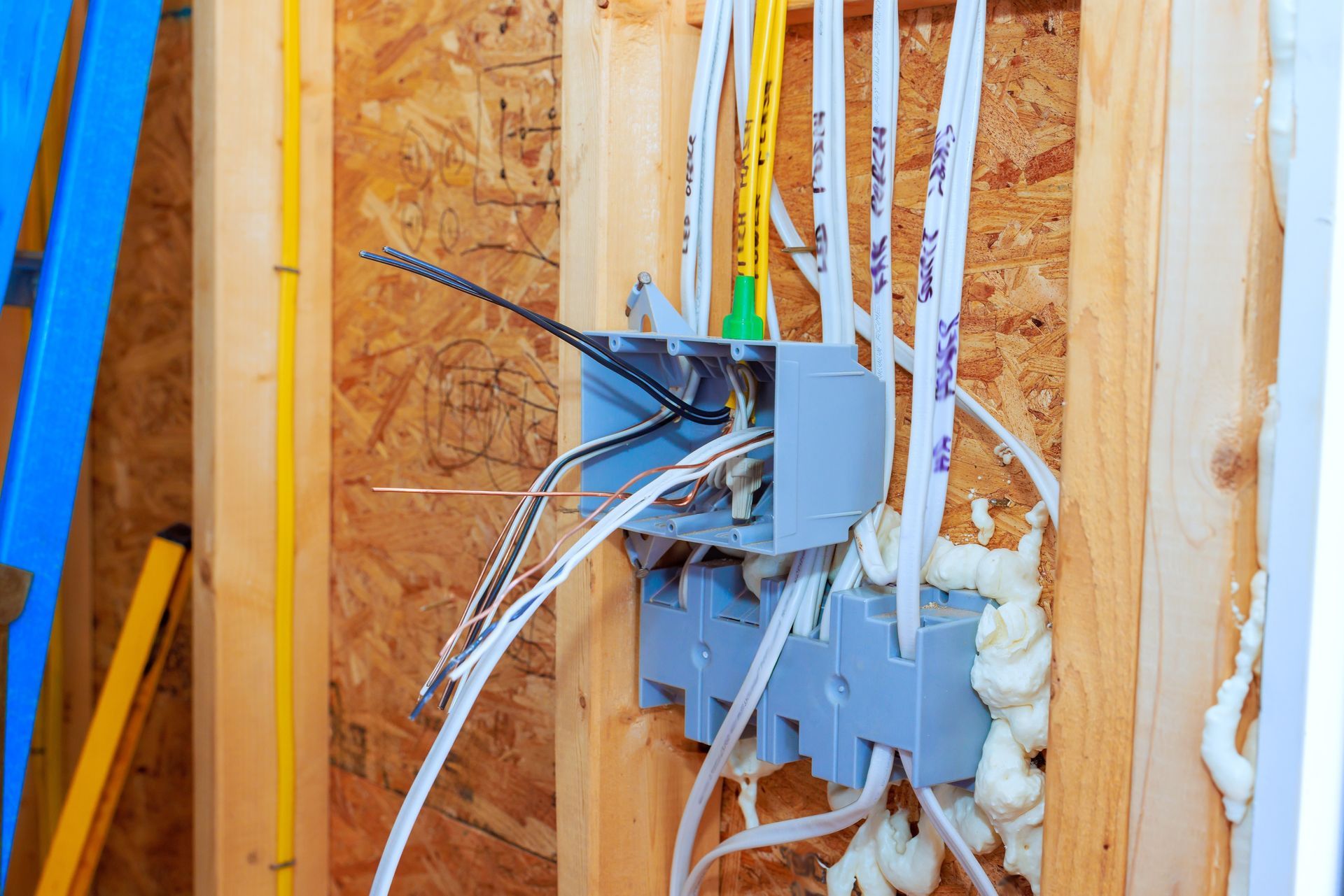 Electrical outlet box with exposed wires and foam insulation in a wooden wall frame