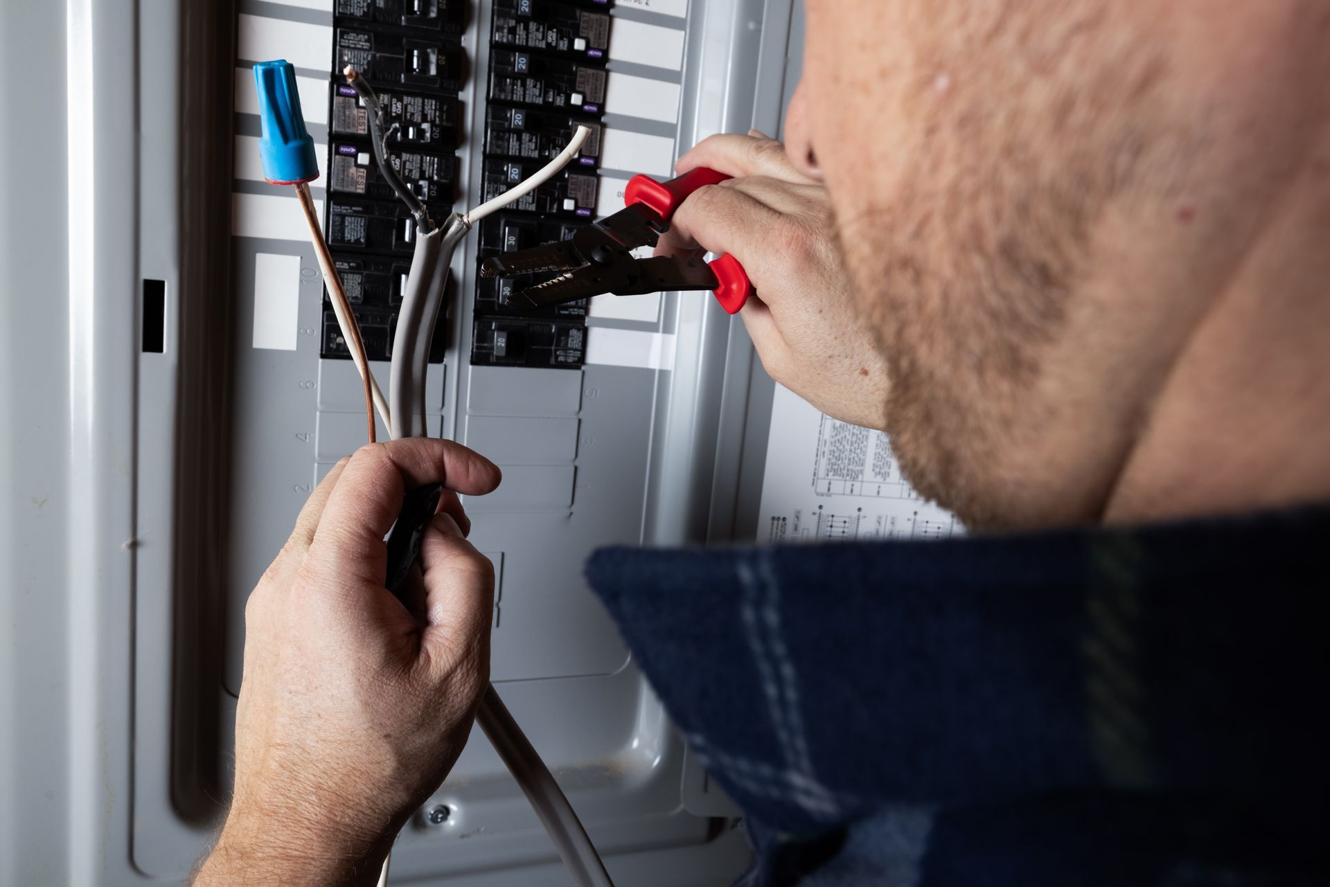 Electrician testing a breaker panel with a multimeter and red-handled tool