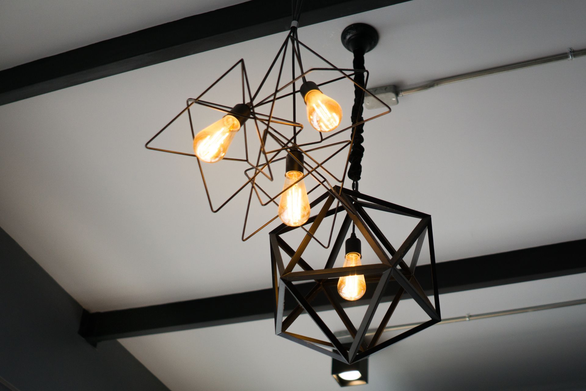 Geometric black pendant light fixture with warm bulbs hanging from a white ceiling