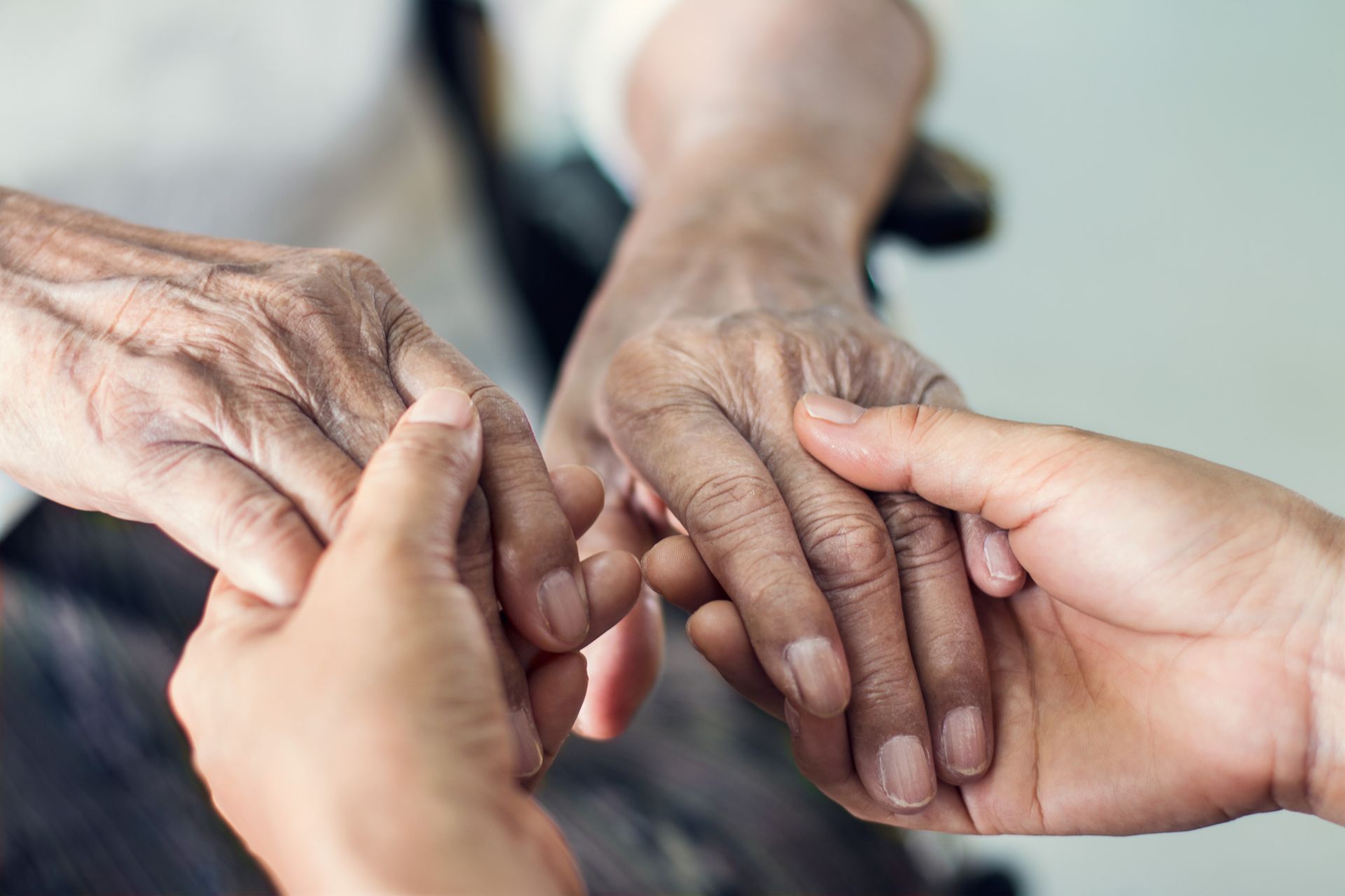 Two pairs of hands gently holding and supporting the hands of an elderly person. Two pairs of hands gently holding and supporting the hands of an elderly person.