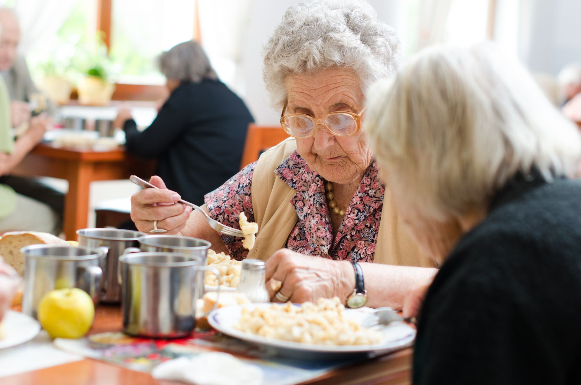 Two people eating at a table with metal mugs and plates of food in a dining area.
