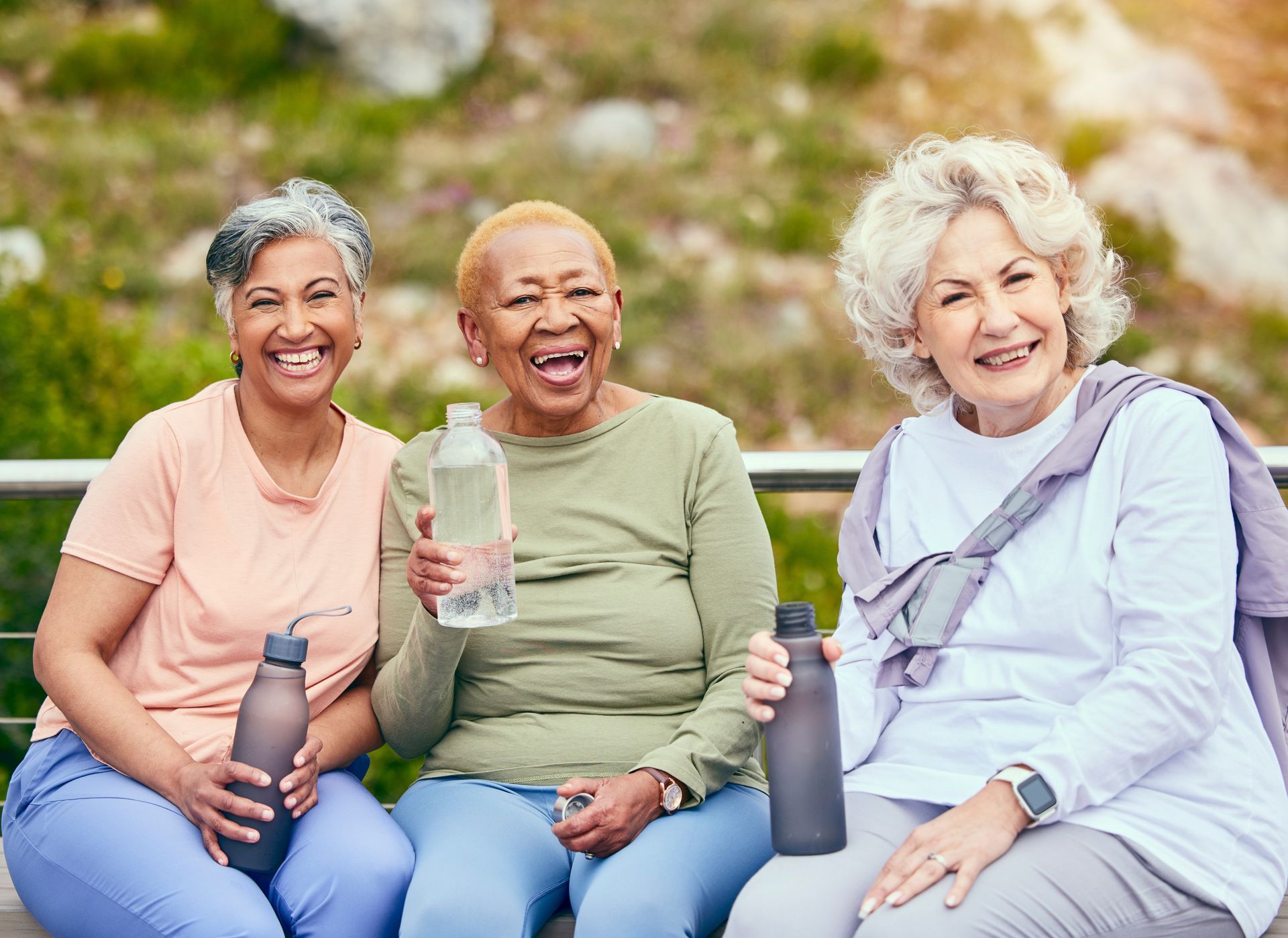 Three women outdoors, smiling, holding water bottles, and seated.