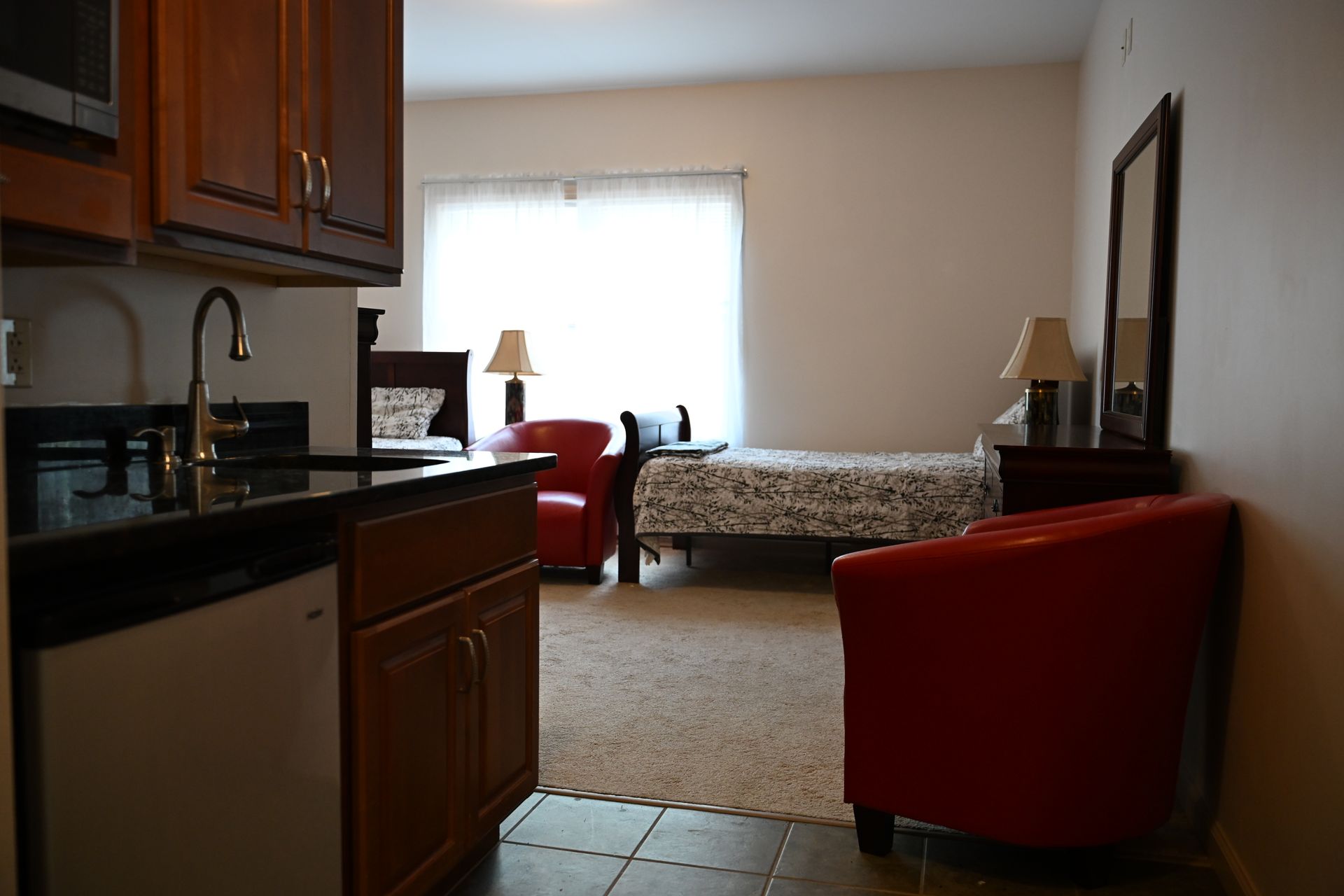 Small apartment with kitchenette and living area; red chairs, bed, and dark cabinetry.