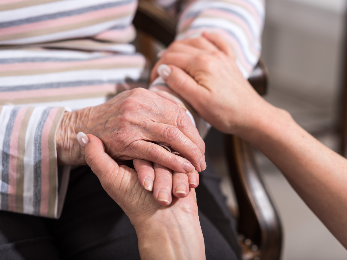Hands of an elderly person being held by another person, providing support and care.
