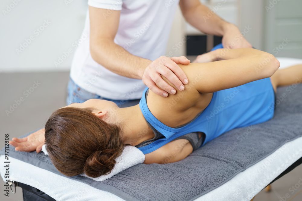 Physiotherapeut streckt den Arm einer Frau, die auf einem Behandlungstisch liegt.