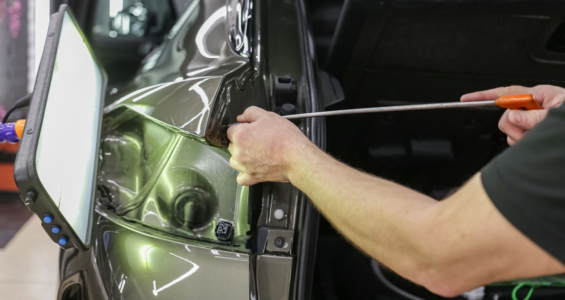 Person using a tool to repair a dent on a dark green car door.