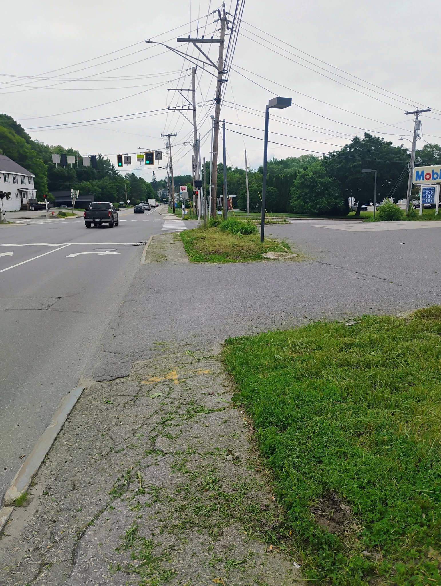 Wide road intersection with cars, utility poles, and a grassy sidewalk on an overcast day