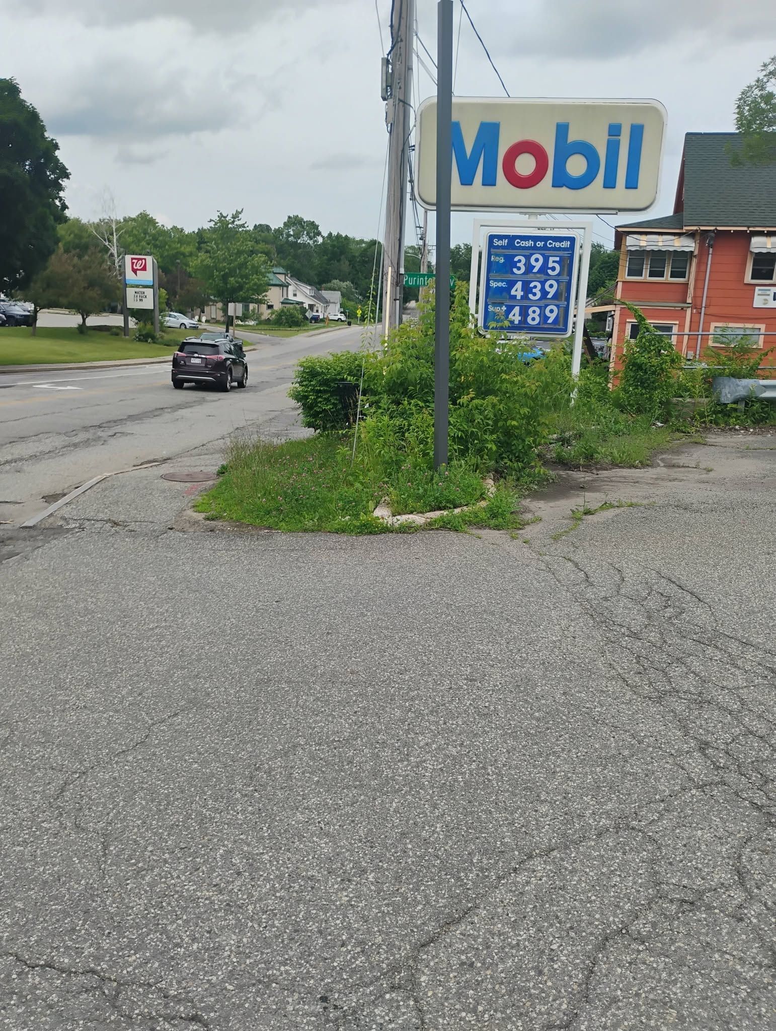 Roadside Mobil gas station sign beside a wet, gravelly road with a passing car and cloudy sky
