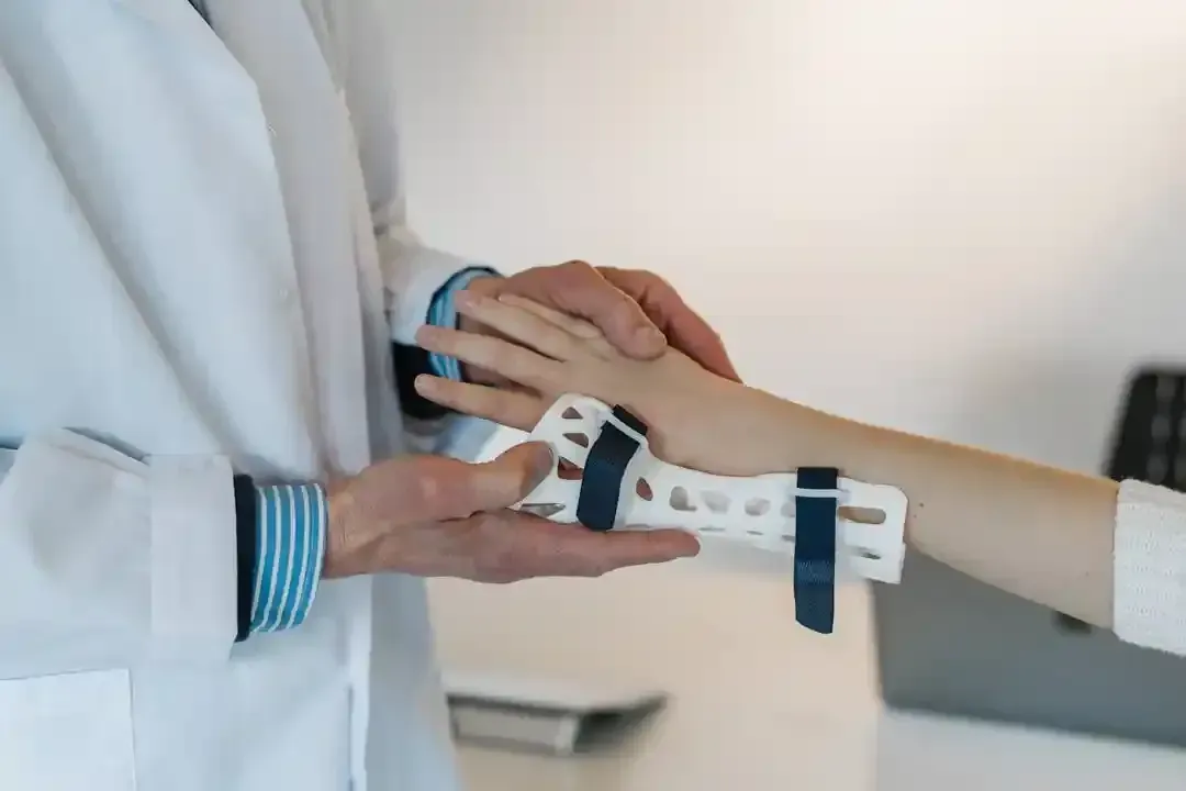 Person fitting a white wrist brace onto another person’s outstretched arm in a clinic.