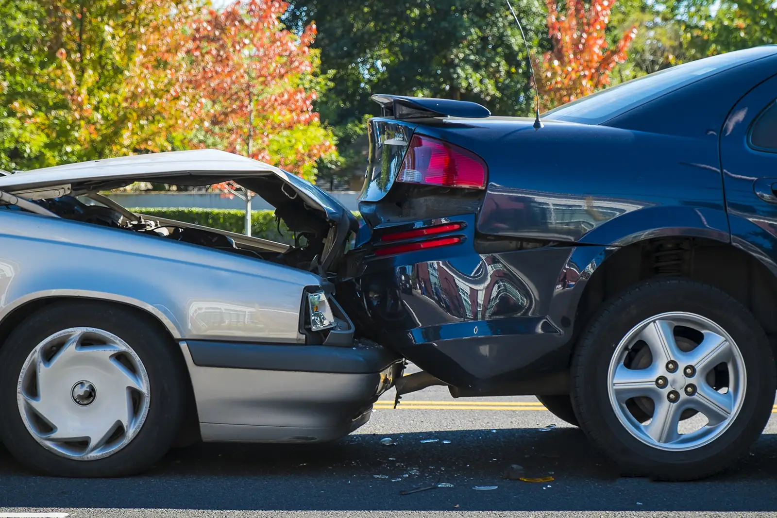 Rear-end car collision between a silver sedan and a black SUV on a road, with damage to both vehicles.