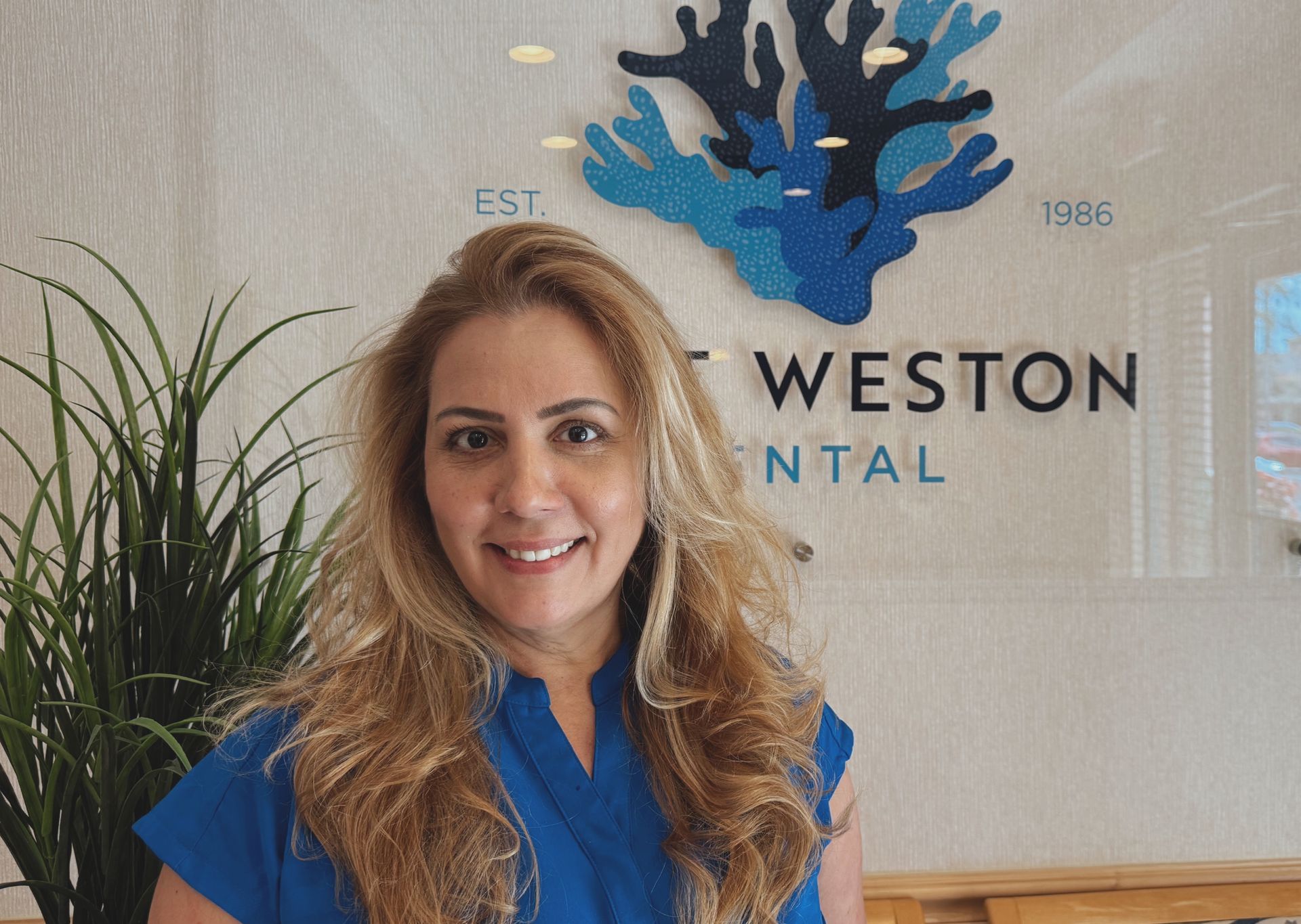 Woman smiling in front of a dental office sign with a coral design.