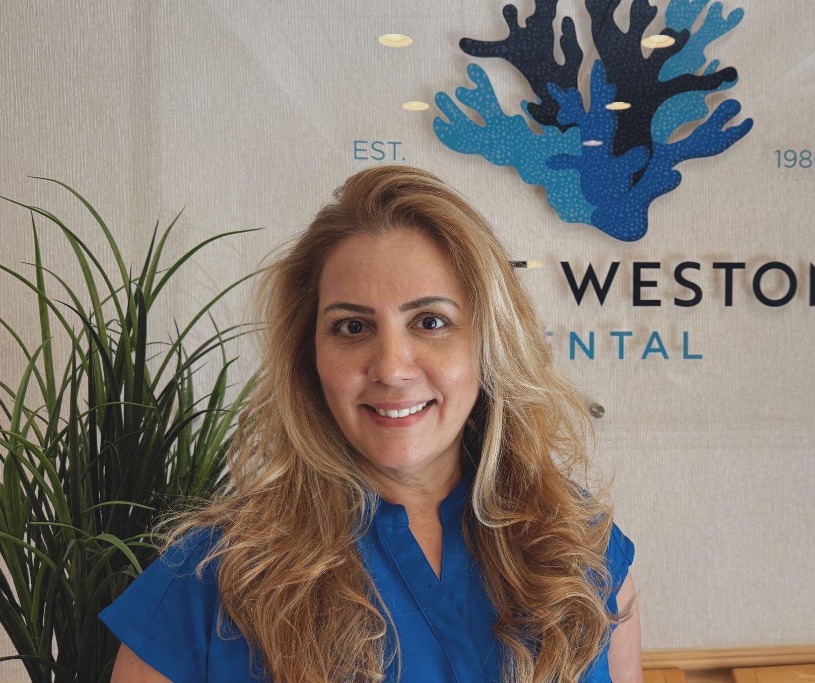 Woman smiling in front of a blue coral logo, wearing a blue shirt.