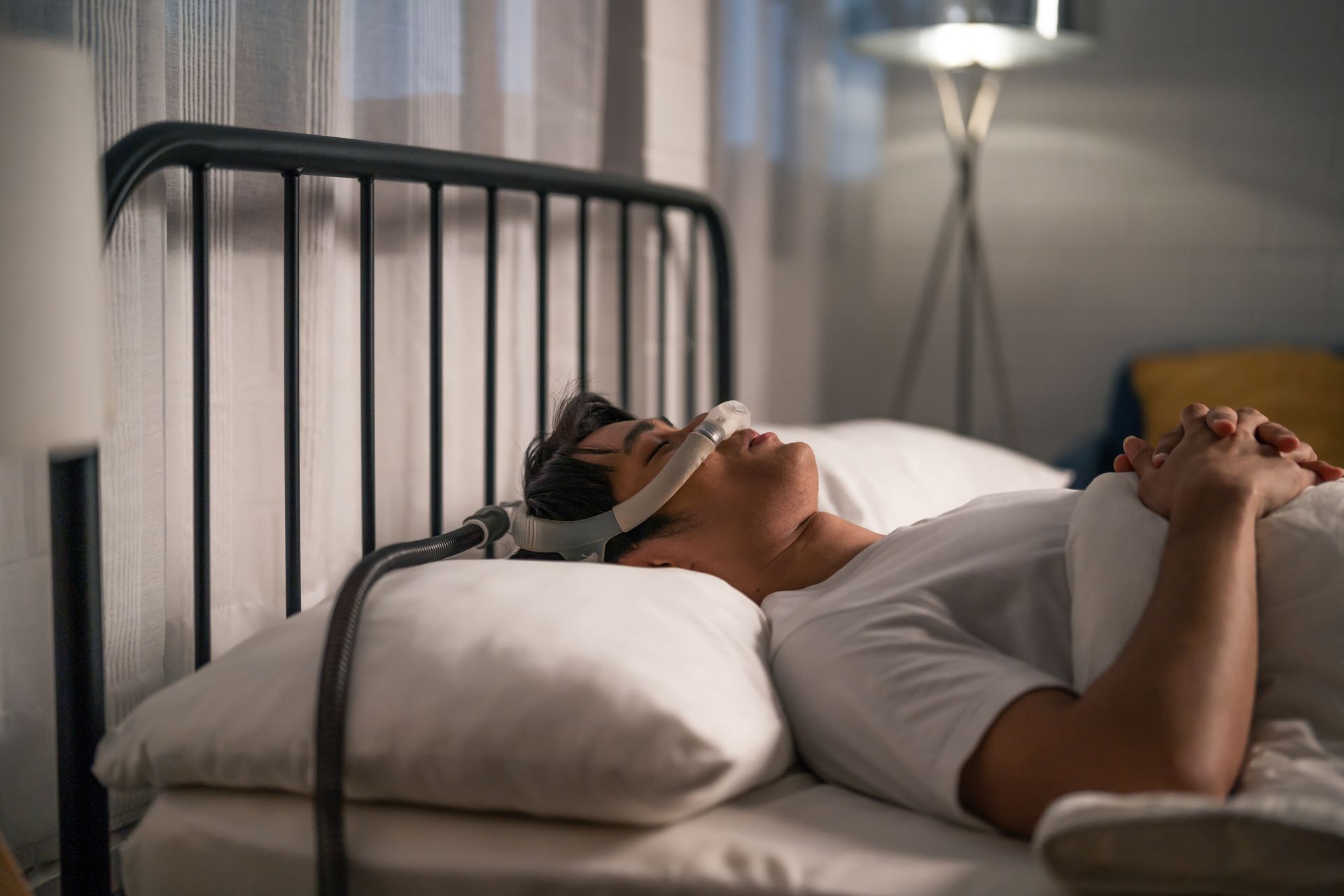 Person lying in bed with a sleep mask, hands clasped, in a softly lit bedroom
