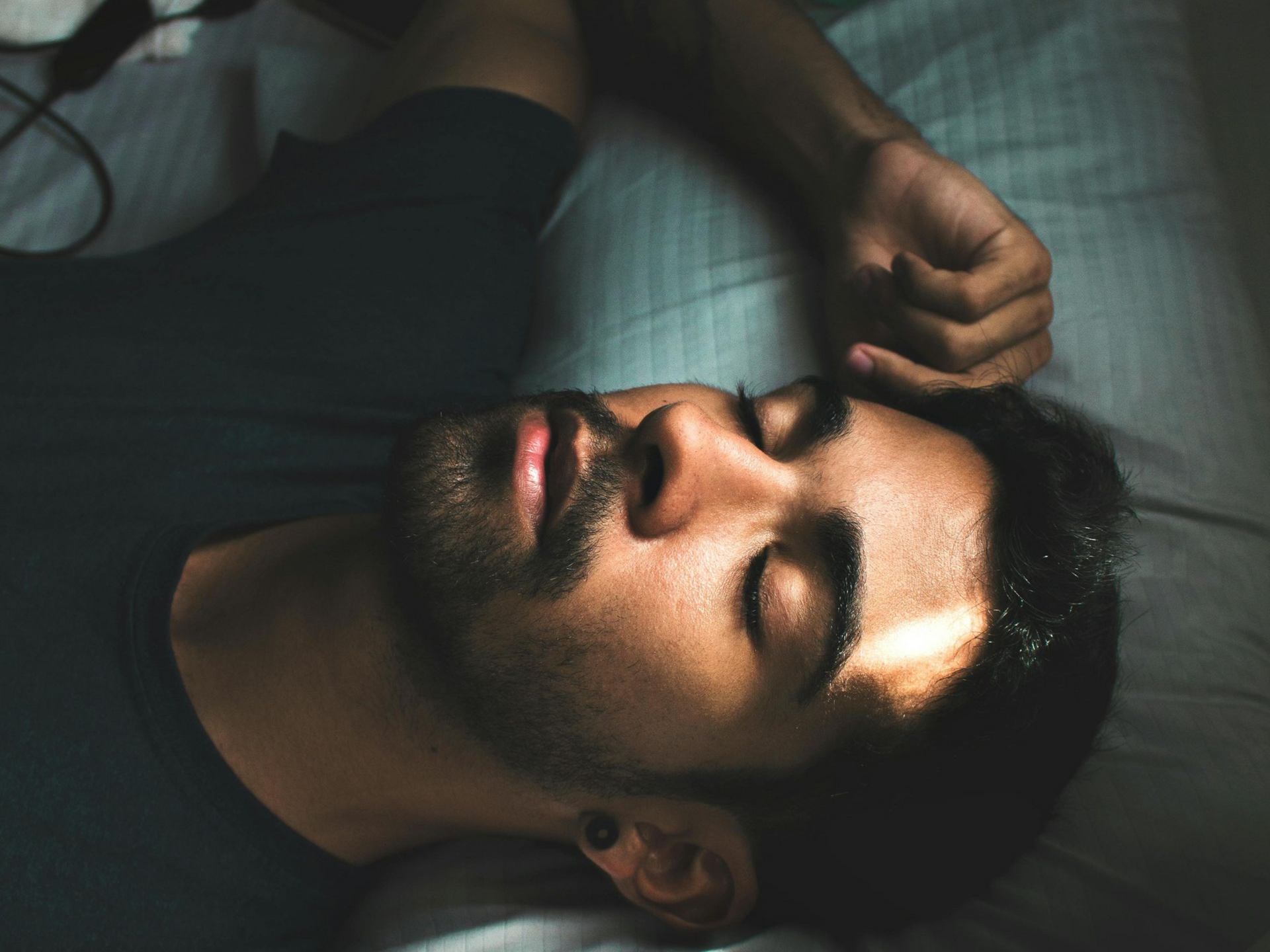 Man wearing a green shirt laying in bed with striped sheets and pillowcase