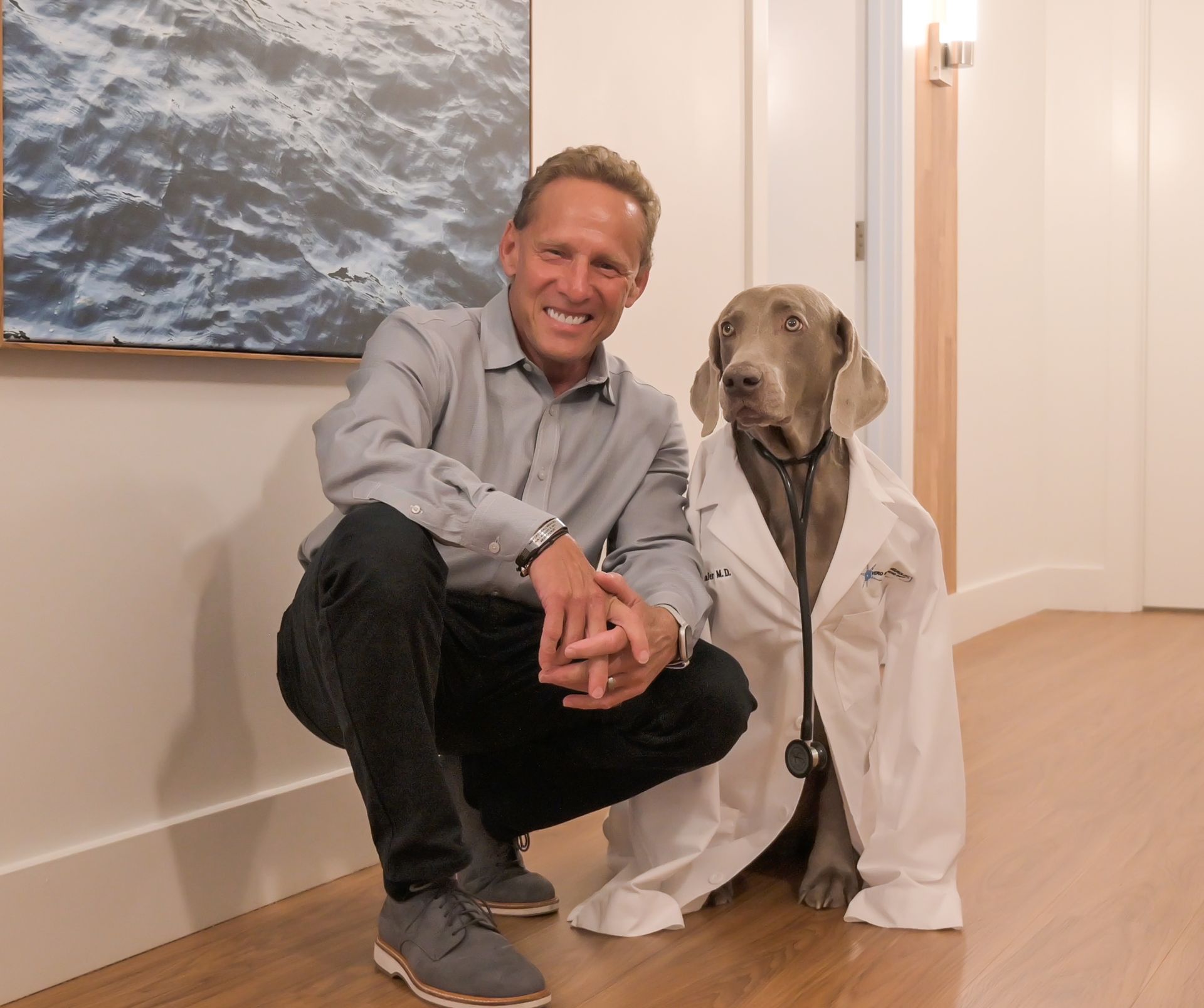 A man is kneeling next to a dog wearing a lab coat