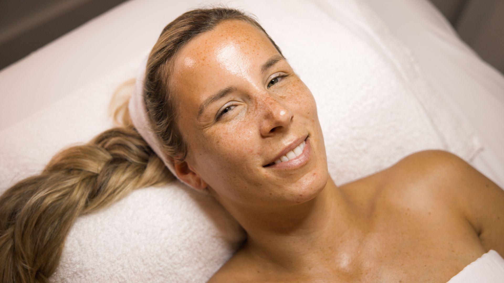 Woman with freckles smiles while lying on a spa bed with a long braid.