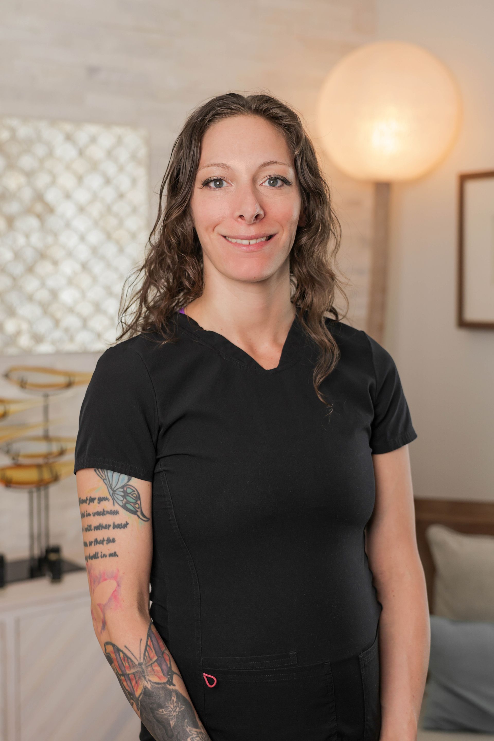 A woman with tattoos on her arm is wearing a black shirt and smiling.