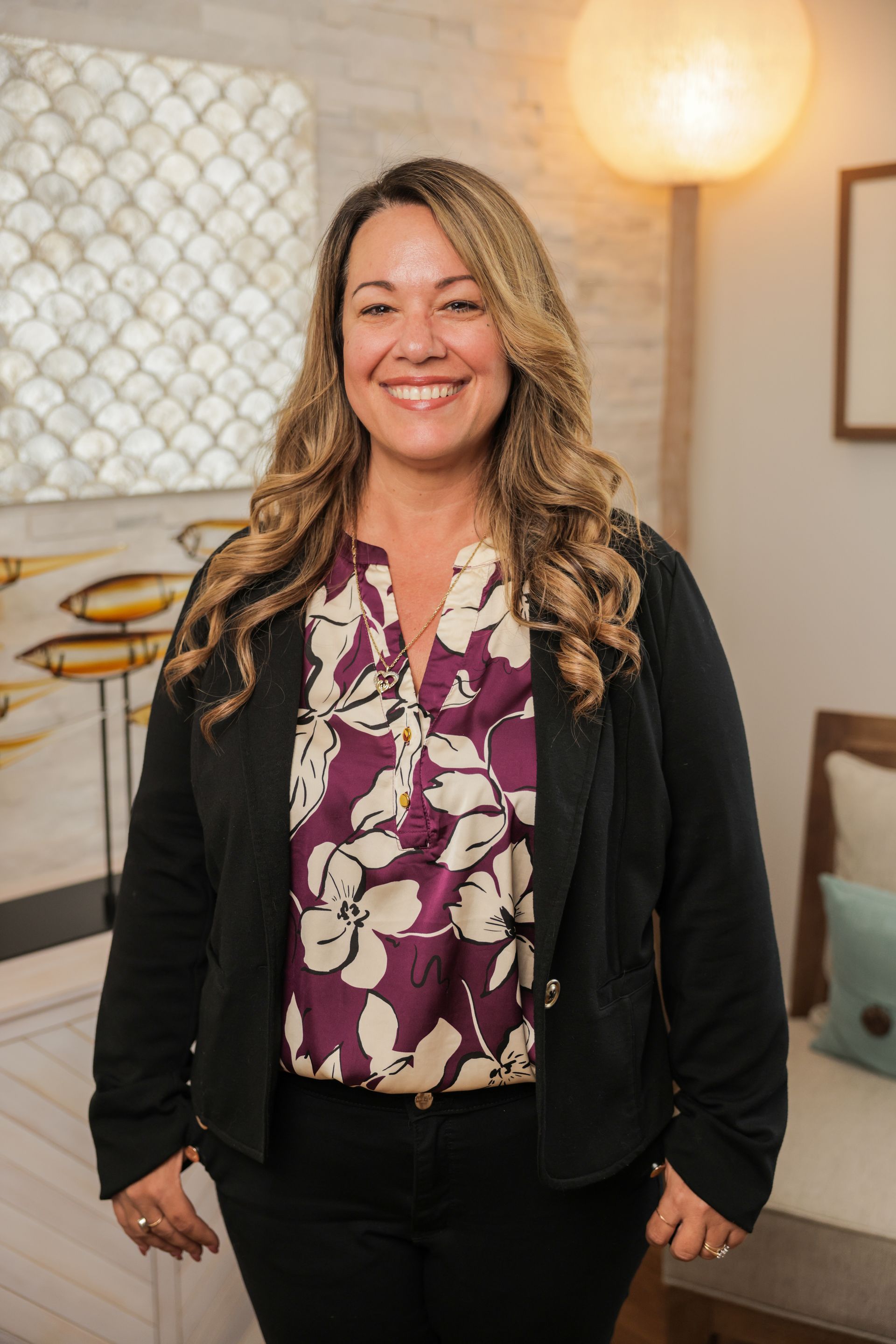 A woman in a black scrub top is smiling in a living room.