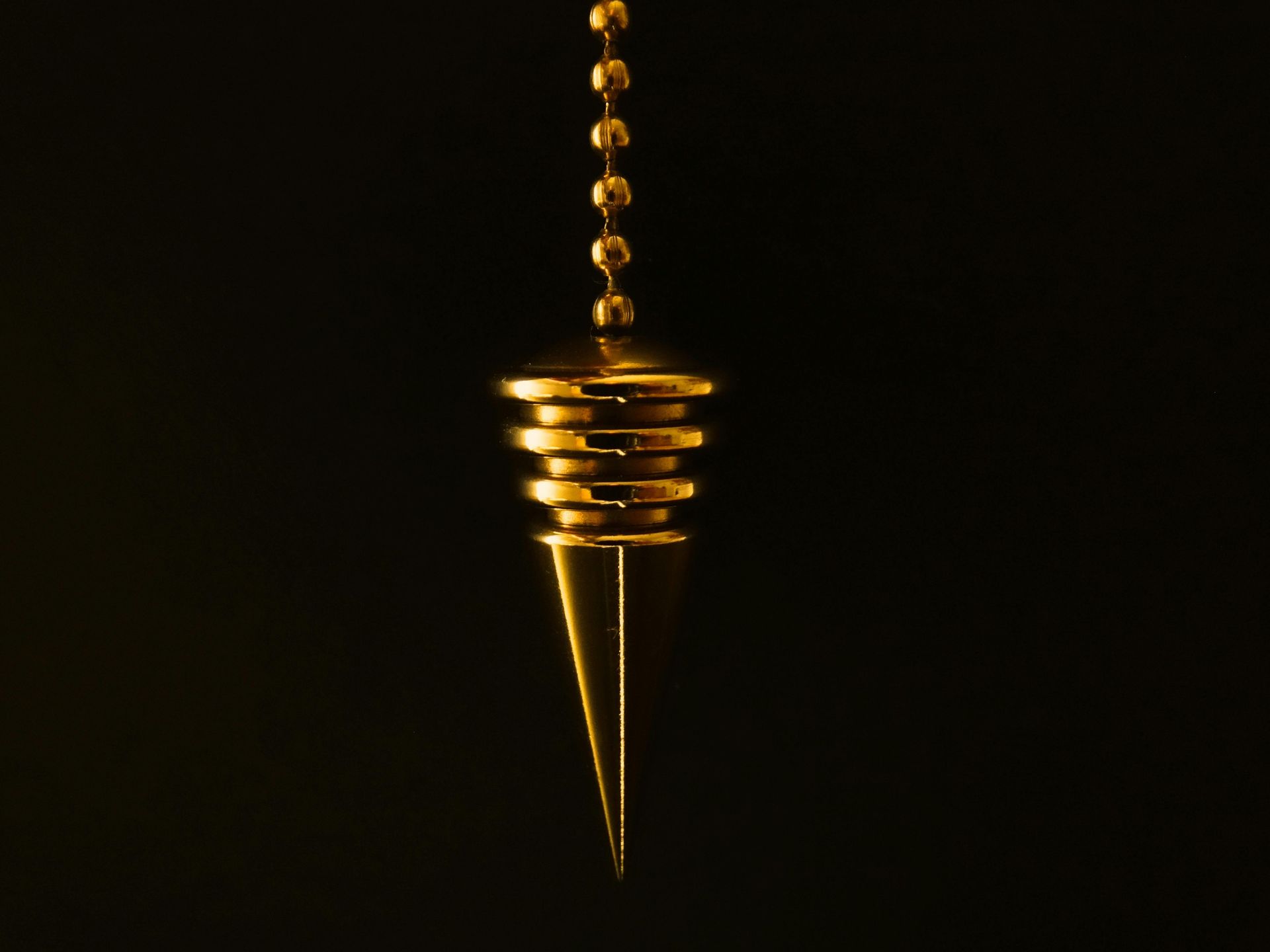 A gold pendulum is hanging from a chain on a black background.