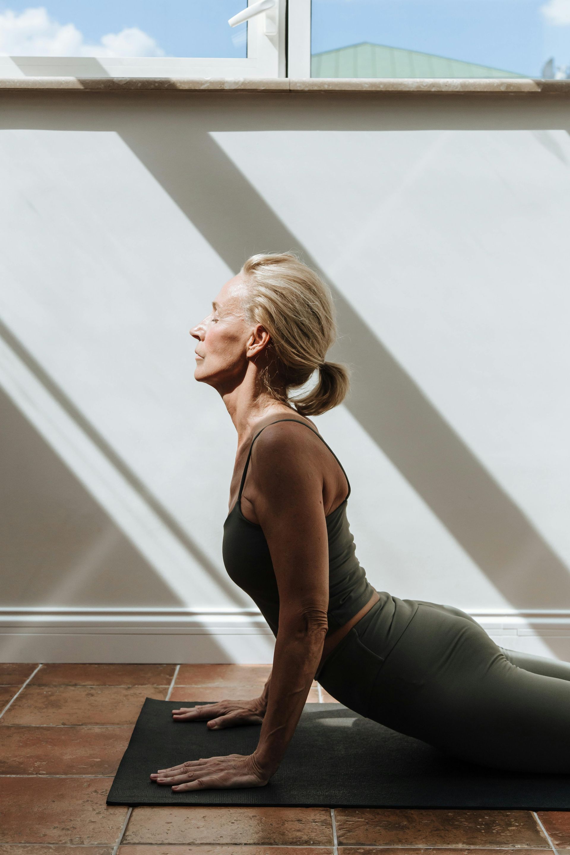 Woman in yoga pose on mat, inside, with sunlight.