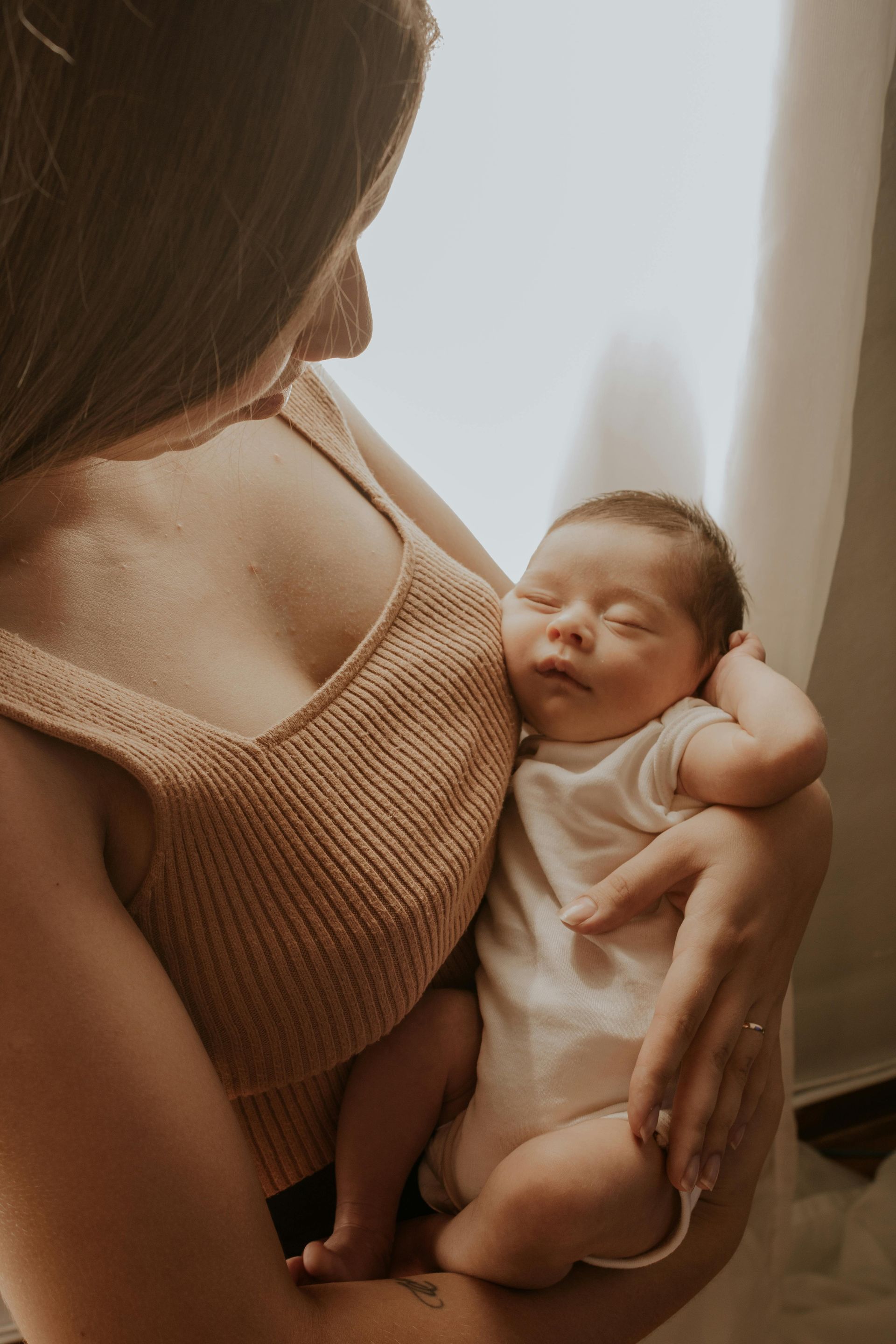 A woman is holding a newborn baby in her arms in front of a window.
