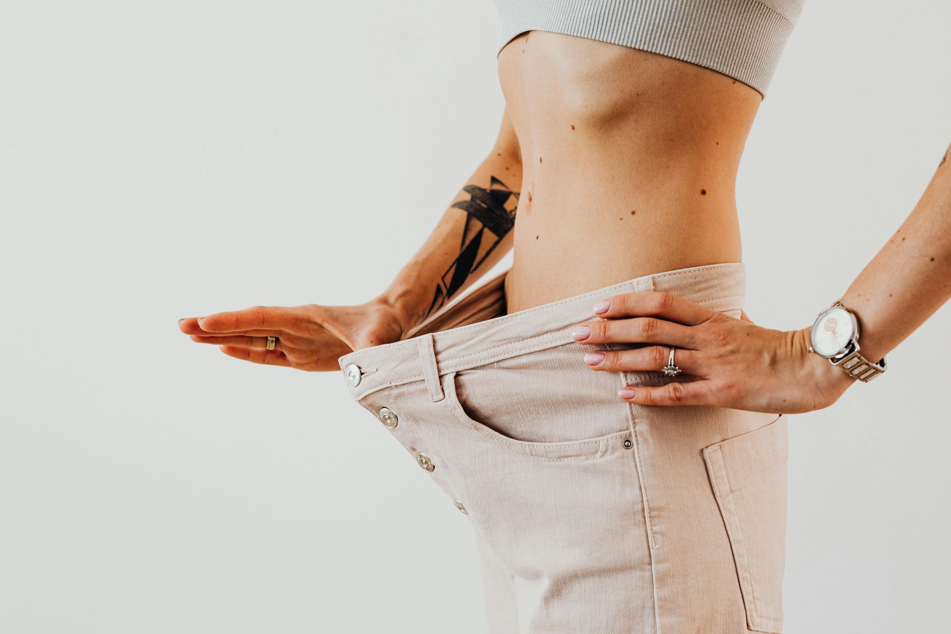 A woman with a tattoo on her arm is holding her pants up.