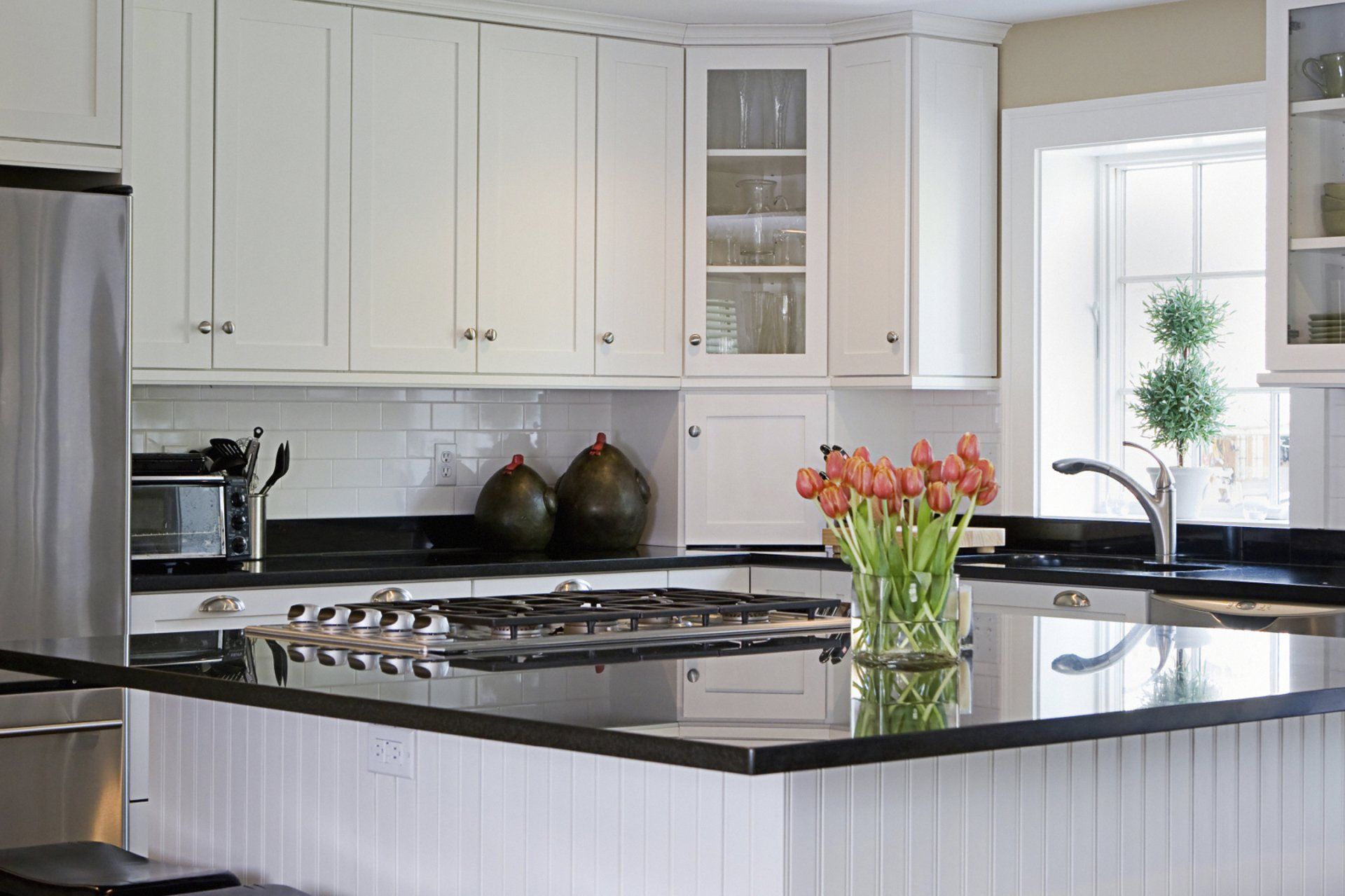 A kitchen with white cabinets and black counter tops and a vase of flowers on the counter.