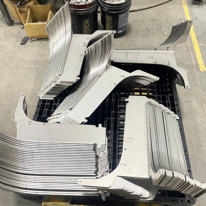 Stacks of gray metal vehicle parts on a black pallet, in a factory setting.
