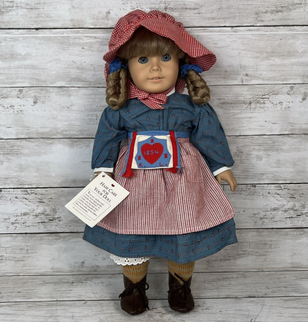 An american girl doll is standing on a wooden table.