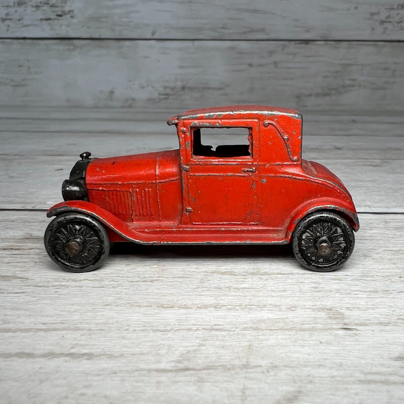 A red toy car is sitting on a wooden table.