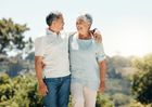 Two people walking side by side outdoors, smiling at each other with their arms around one another.